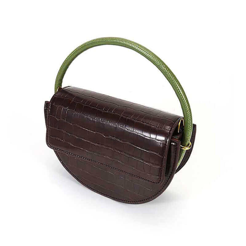 A brown, semi-circle shaped leather handbag with a vibrant green handle, placed on a white surface, angle view