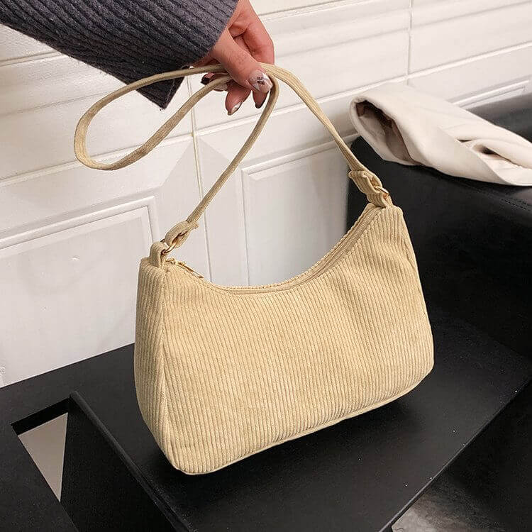 A person holding a Beige corduroy handbag with a shoulder strap.