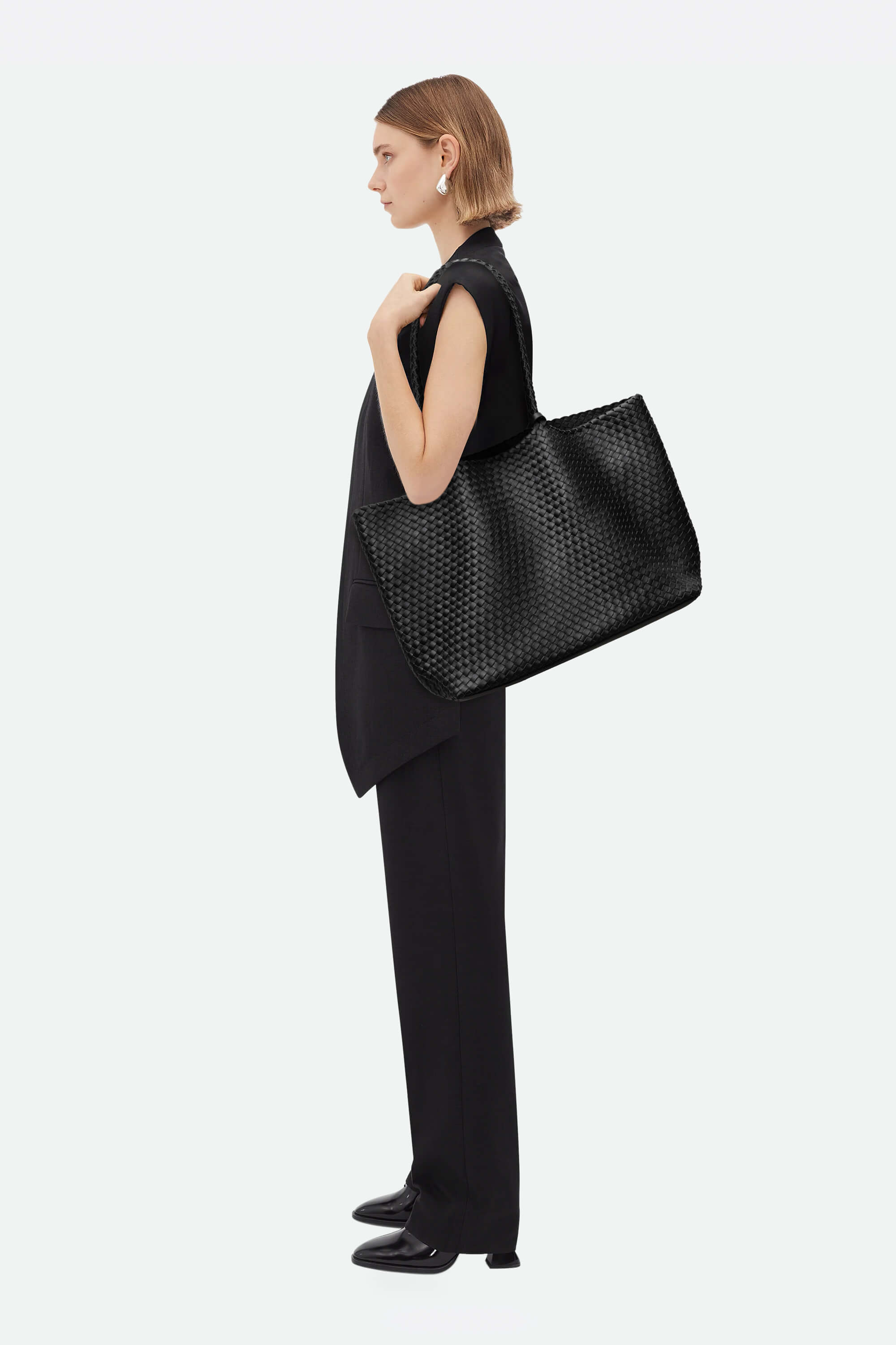 Woman holding a black perforated handbag against a white background