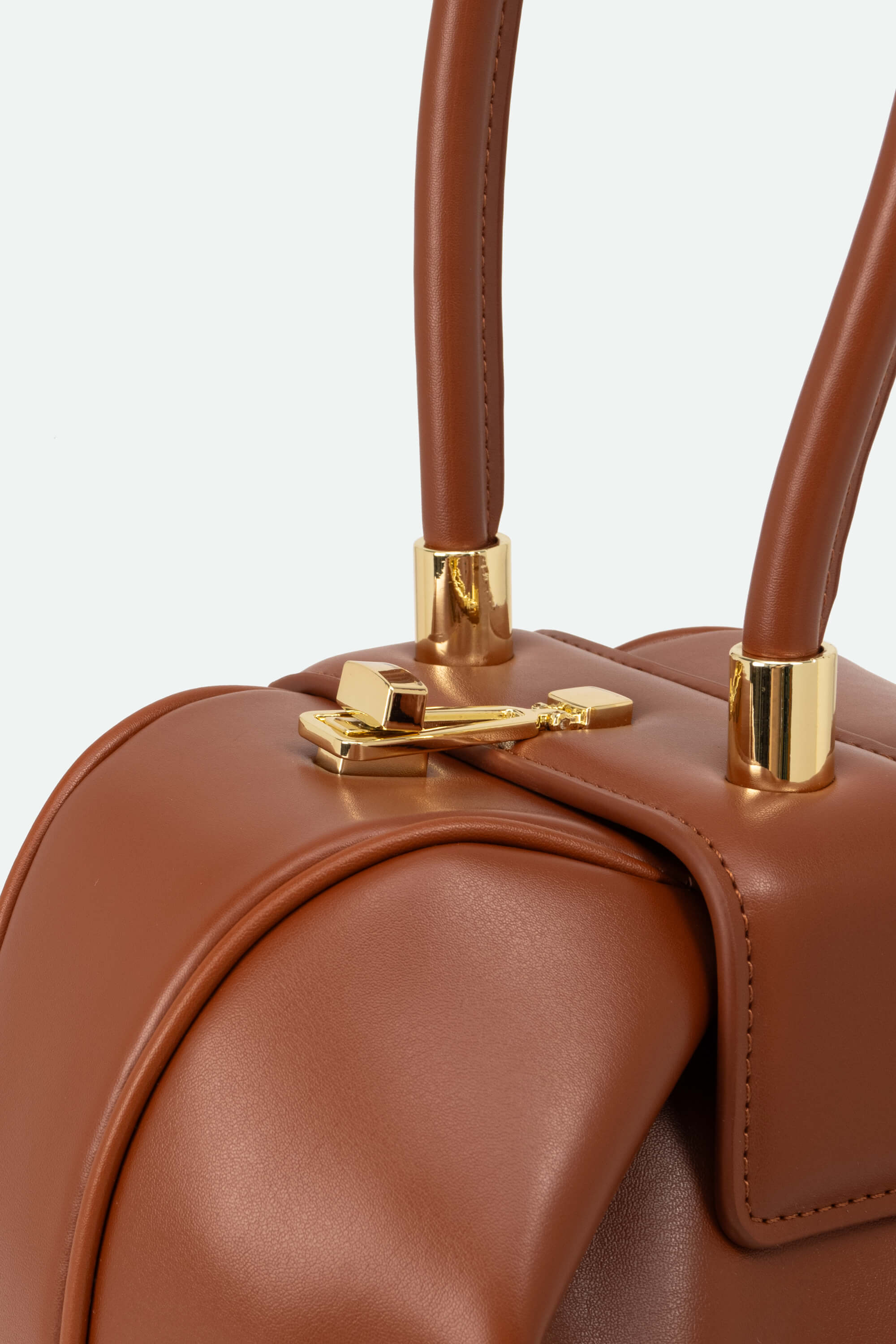 Close-up of a brown leather handbag with gold hardware on a light gray background