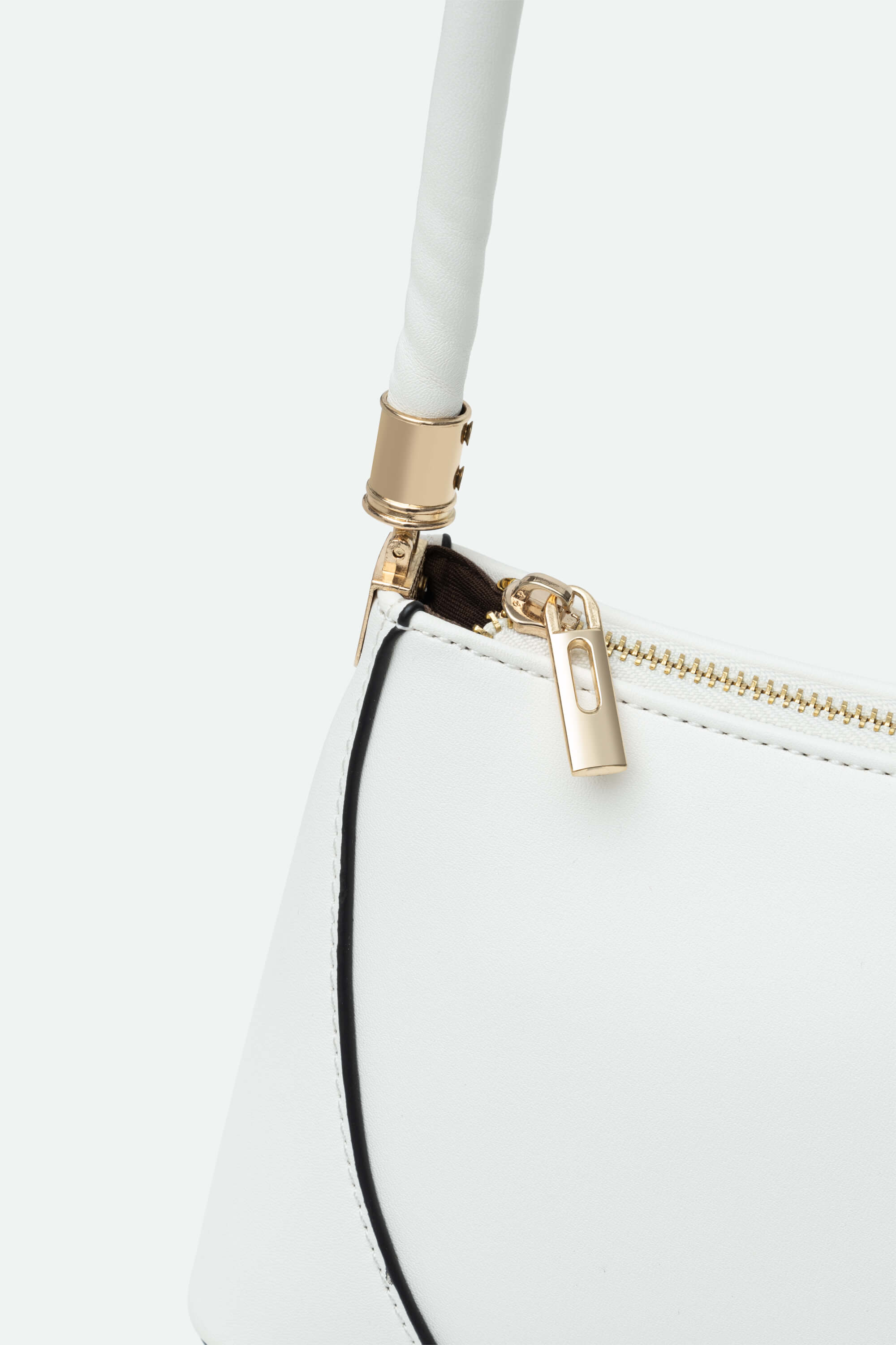 Close-up of a white handbag with gold zipper and black strap on a light gray background