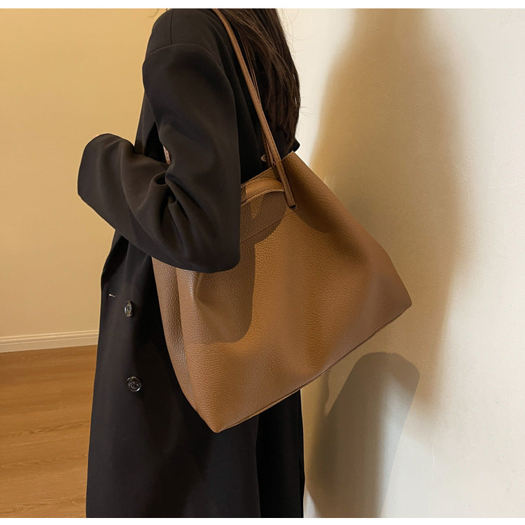 Person wearing a black coat holding a brown leather handbag indoors.