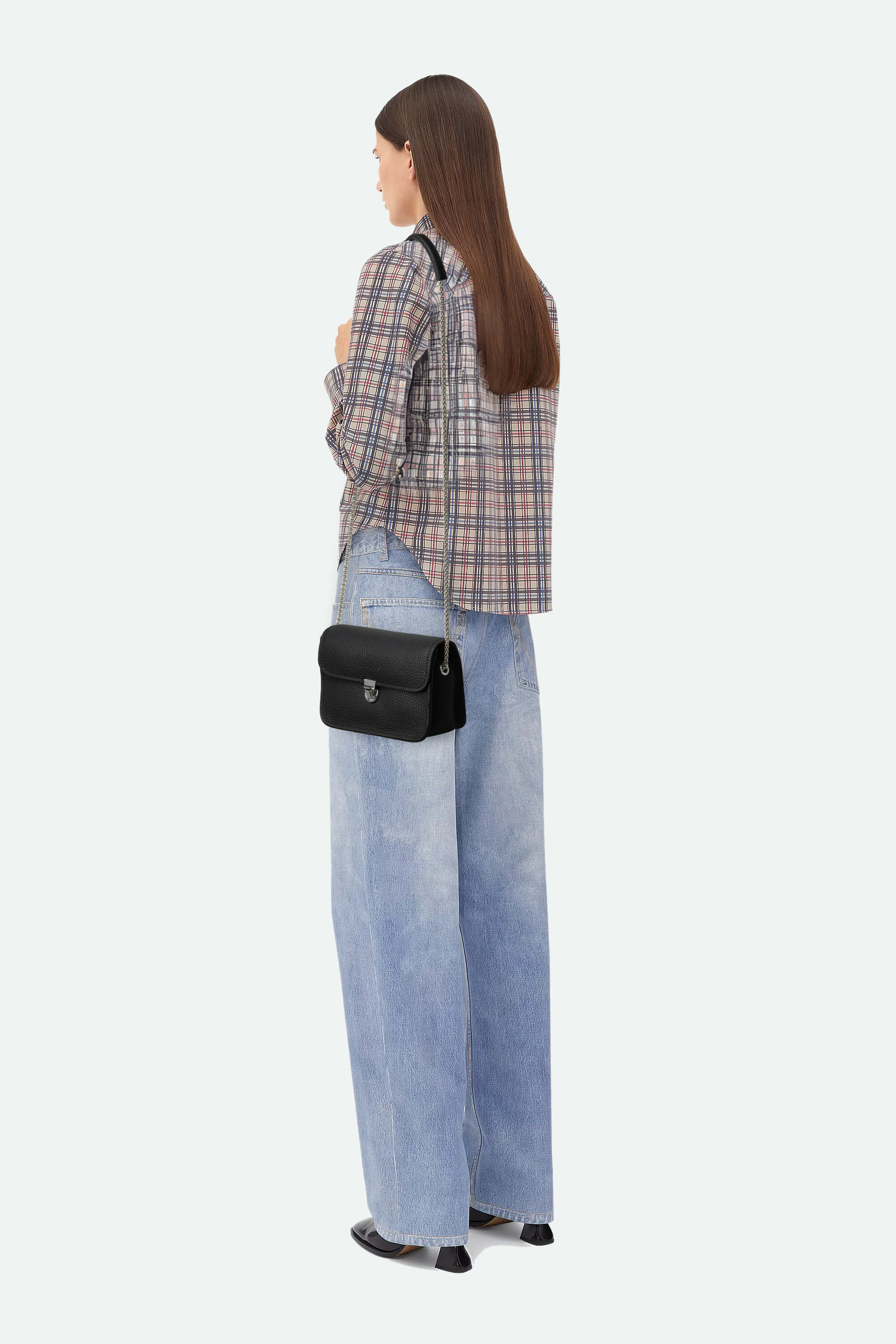 Person wearing a plaid shirt and jeans with a black bag on a white background