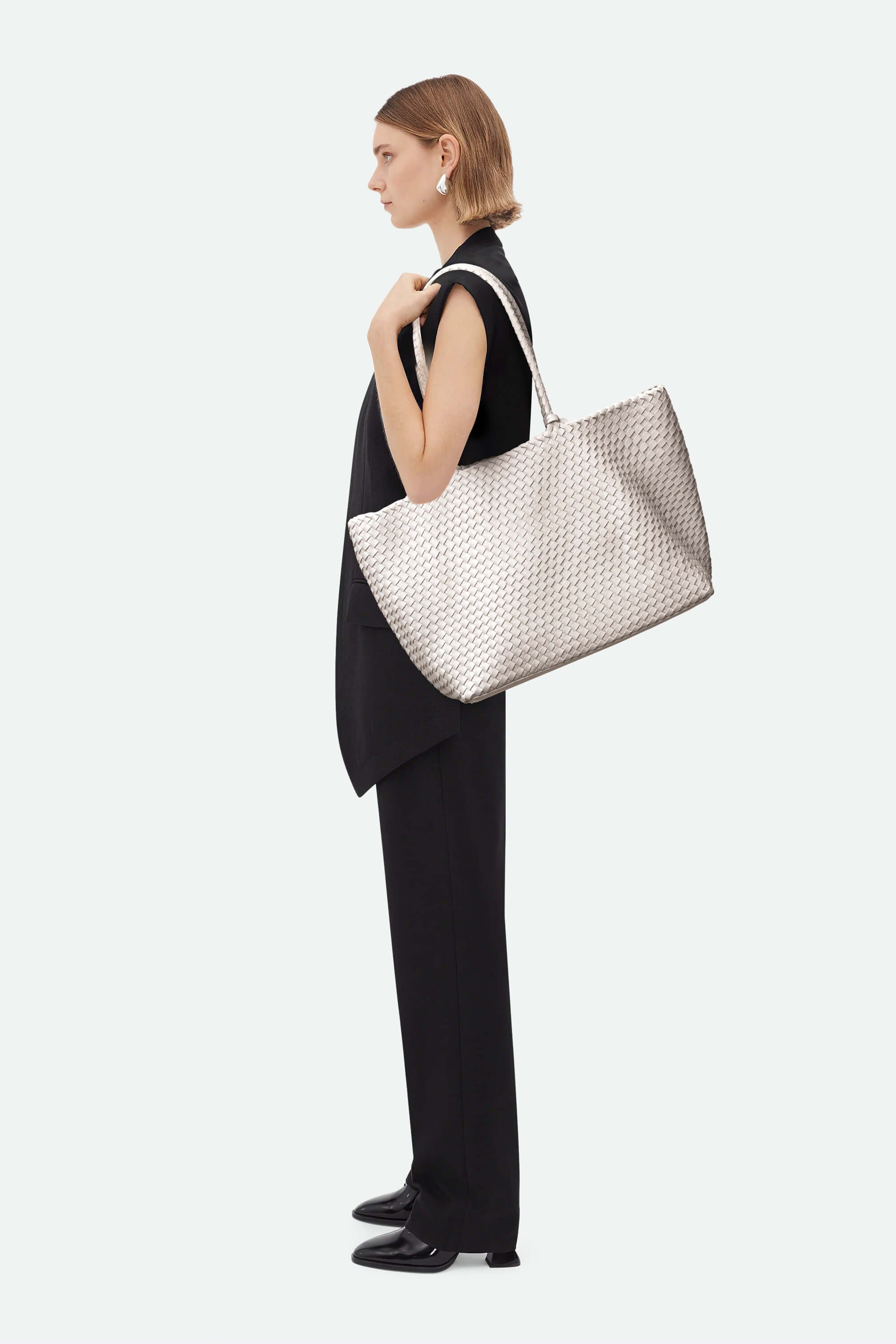 Woman holding a large woven handbag against a white background