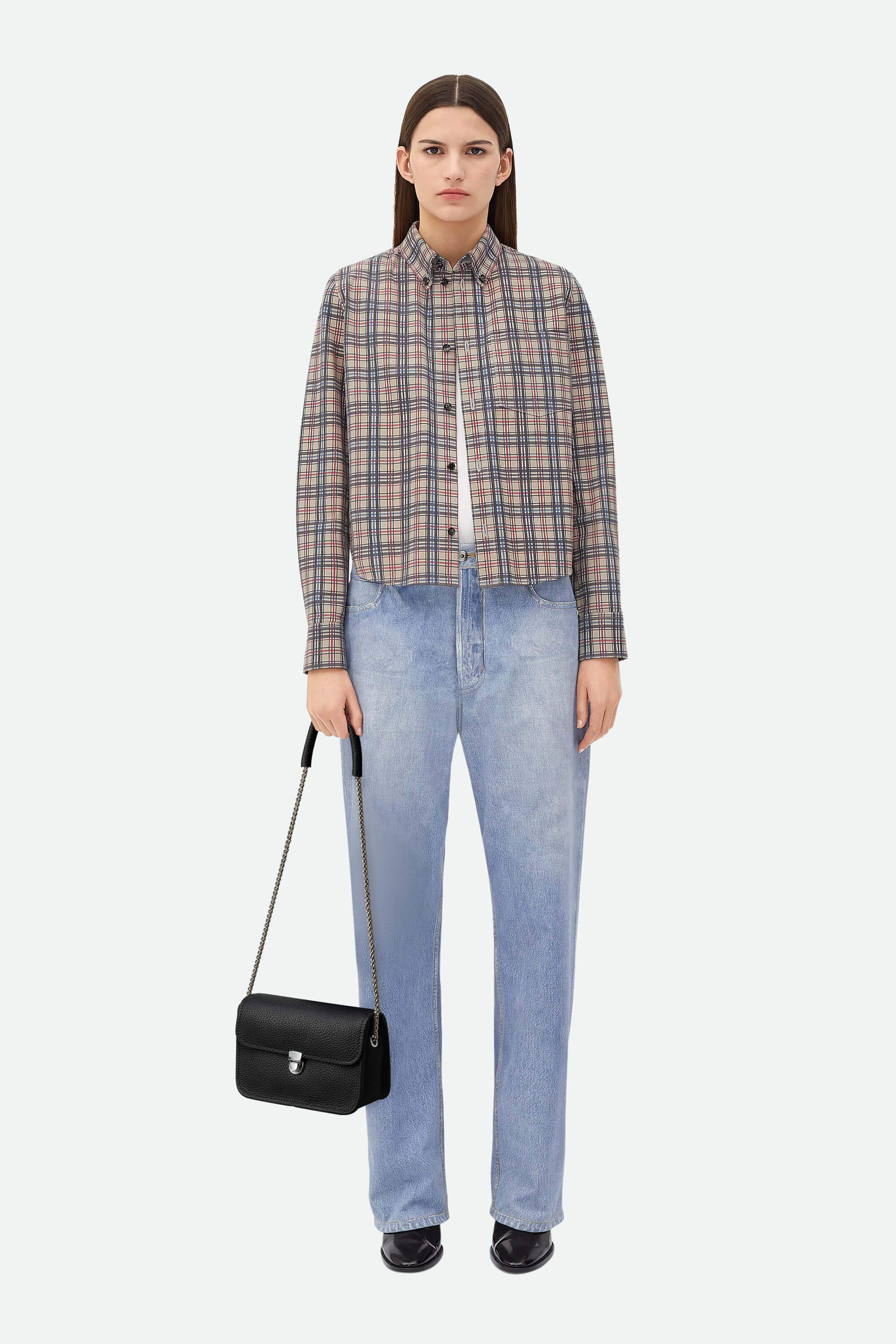 Woman wearing a plaid shirt and blue jeans holding a black handbag on a white background