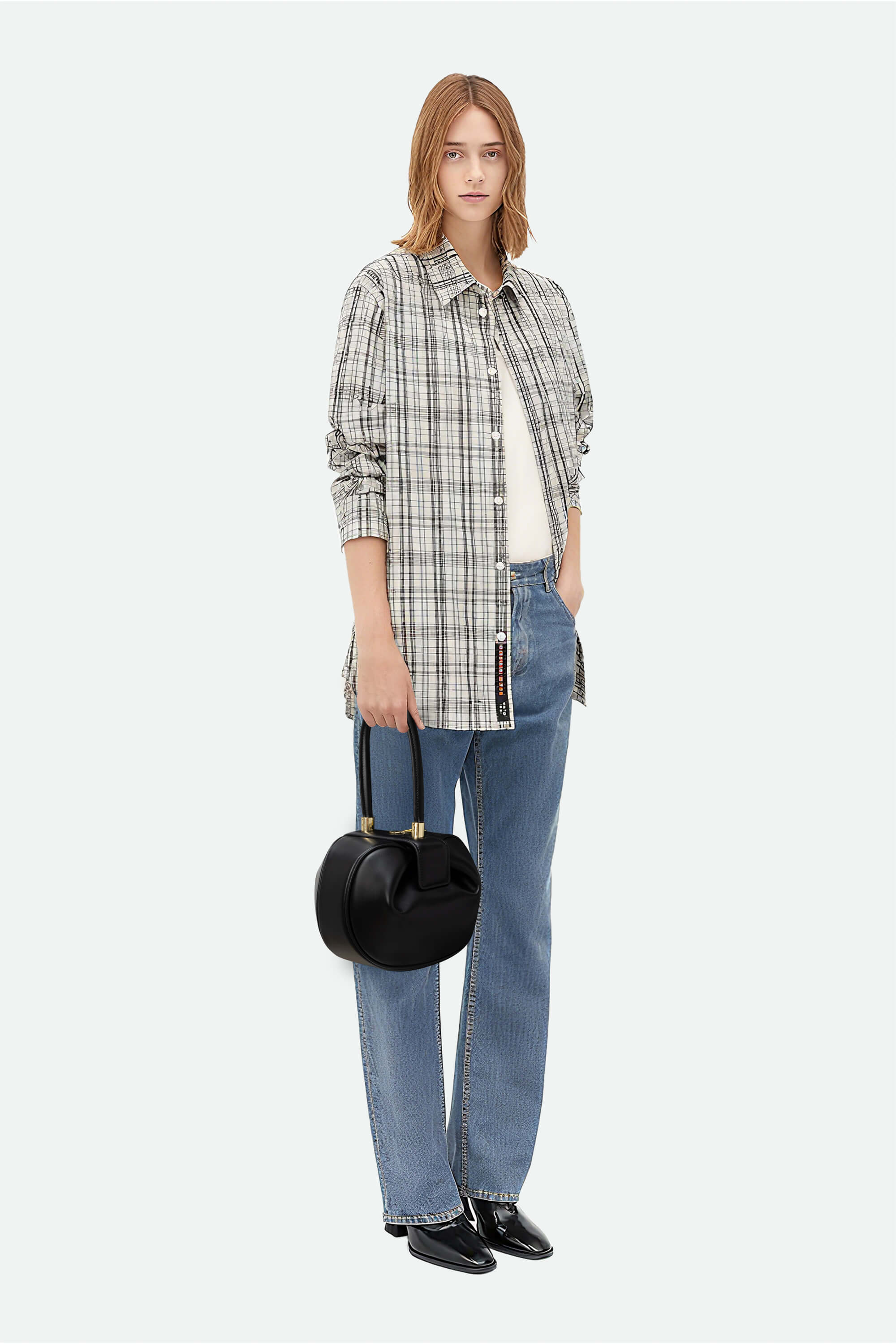 Woman wearing a plaid shirt, jeans, and holding a black handbag on a white background