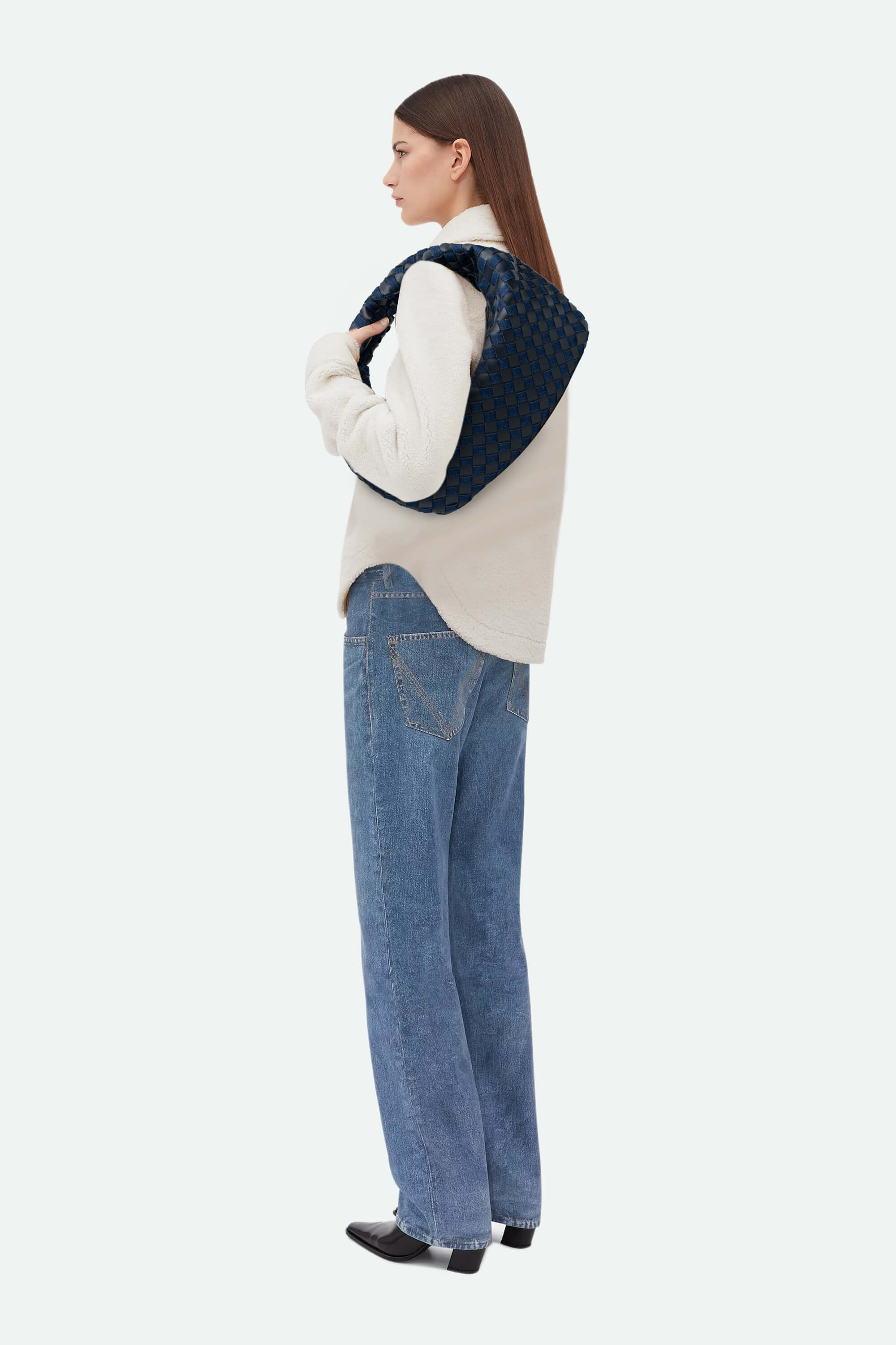 Woman wearing a white sweater, blue denim vest, and jeans on a white background