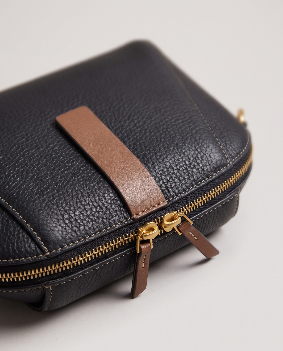 Elara mini leather crossbody in Black – close-up of the tan tab, zips and pebbled leather