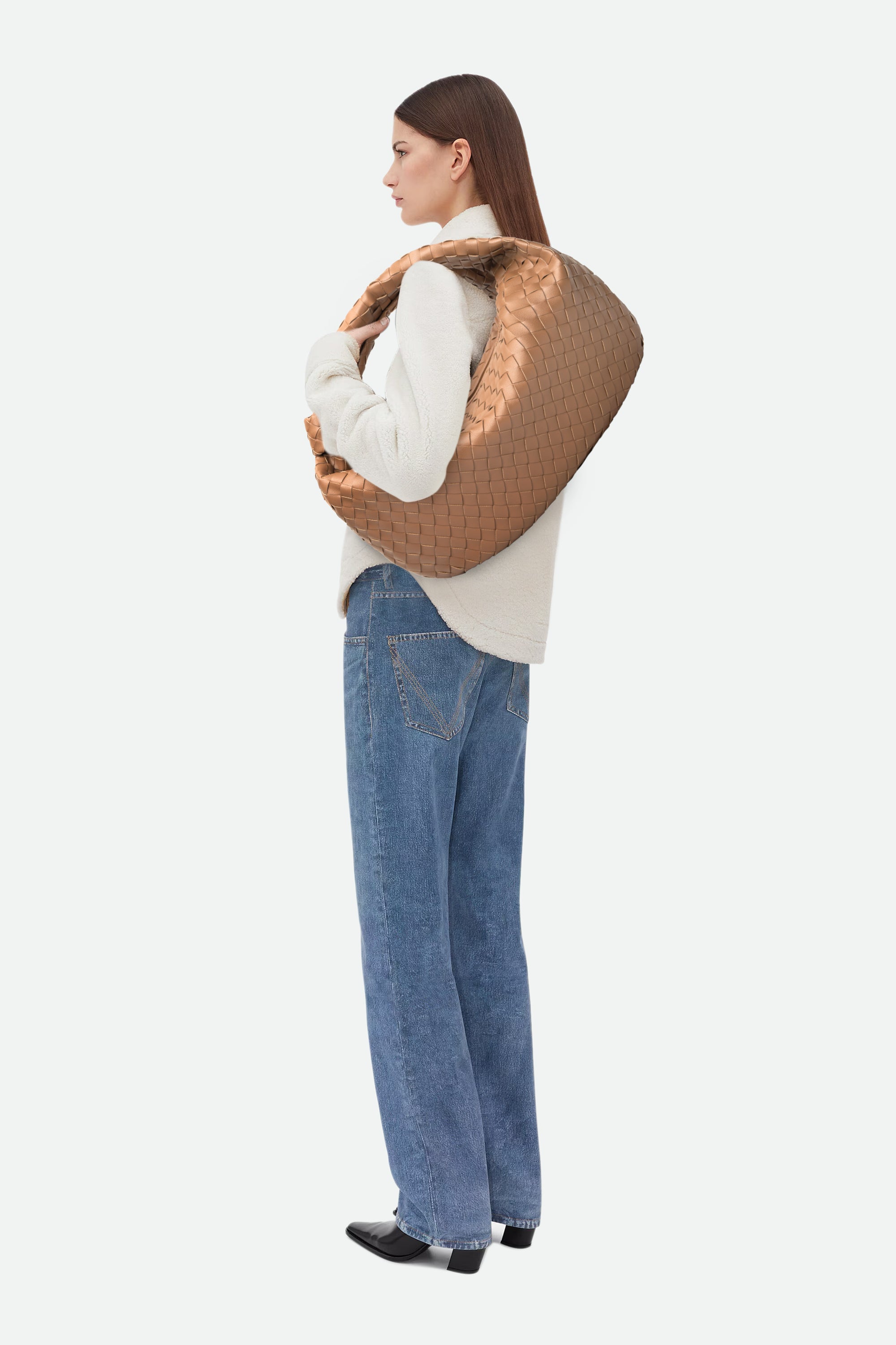 Woman wearing a white sweater and blue jeans carrying Large Knot Bag (Jodie) light brown woven handbag on her shoulder.