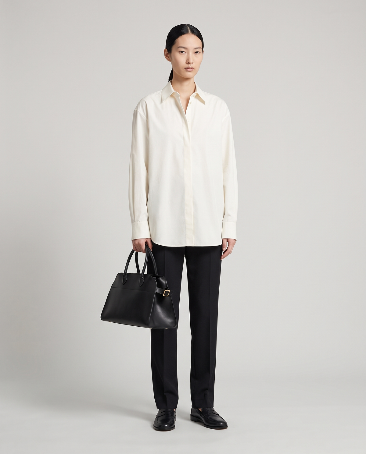 Milano Small top-handle bag in Black – model holding it by the top handles, full length