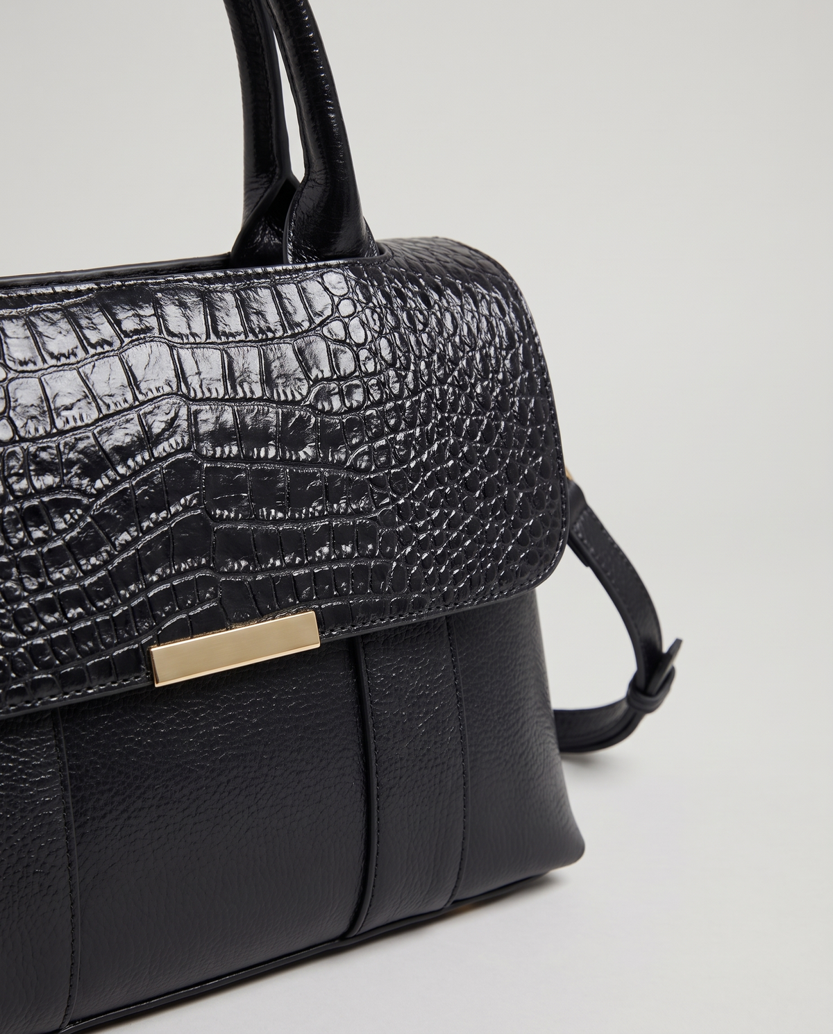 Sloane croc-embossed leather handbag in Black – close-up of the croc flap and gold bar