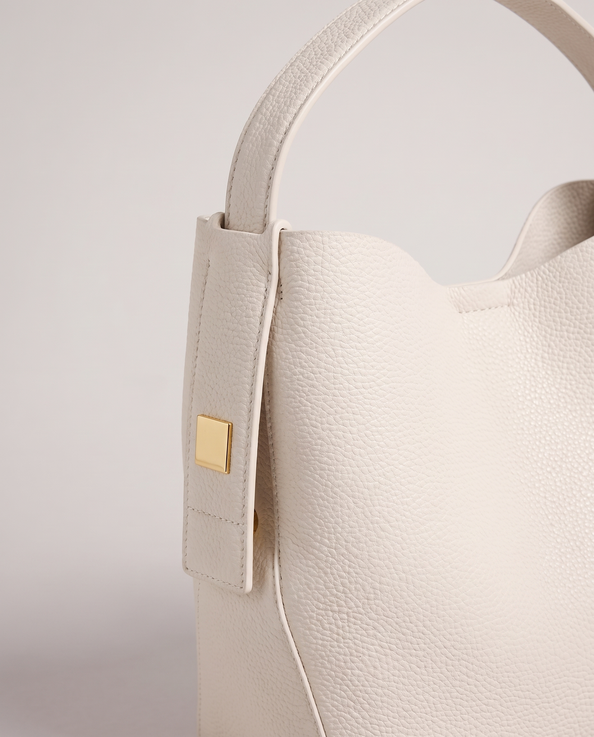 Transit leather bucket bag in Chalk – close-up of the handle tab and gold hardware