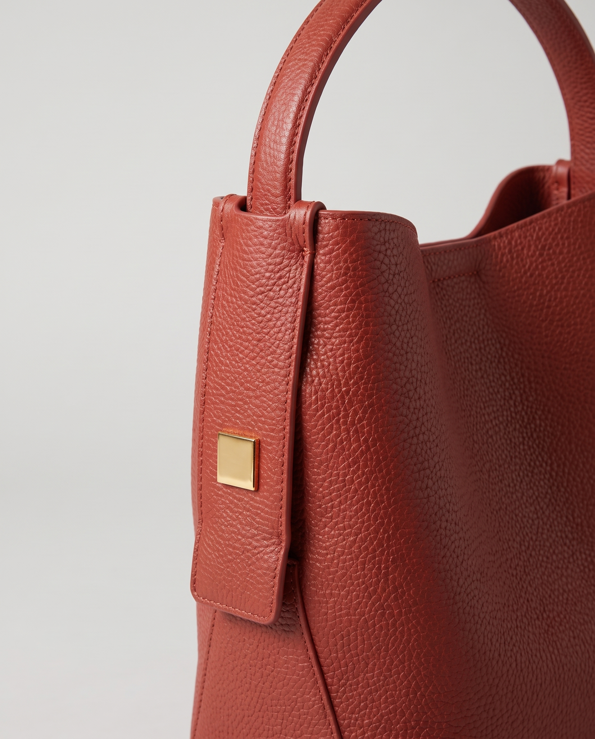Transit leather bucket bag in Rust – close-up of the handle tab and gold hardware