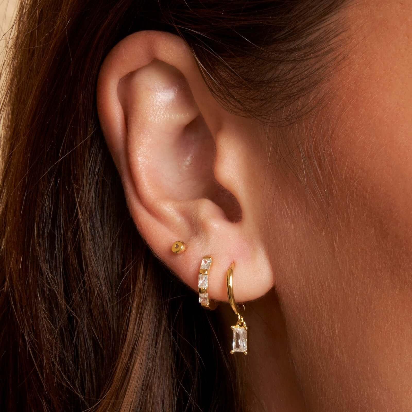 A woman showing her stack of gold charm earrings