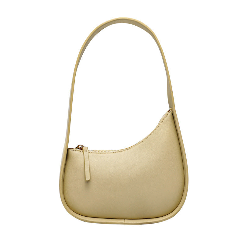 A beige leather shoulder bag with a half moon design, featuring a wide shoulder strap and a soft handle.