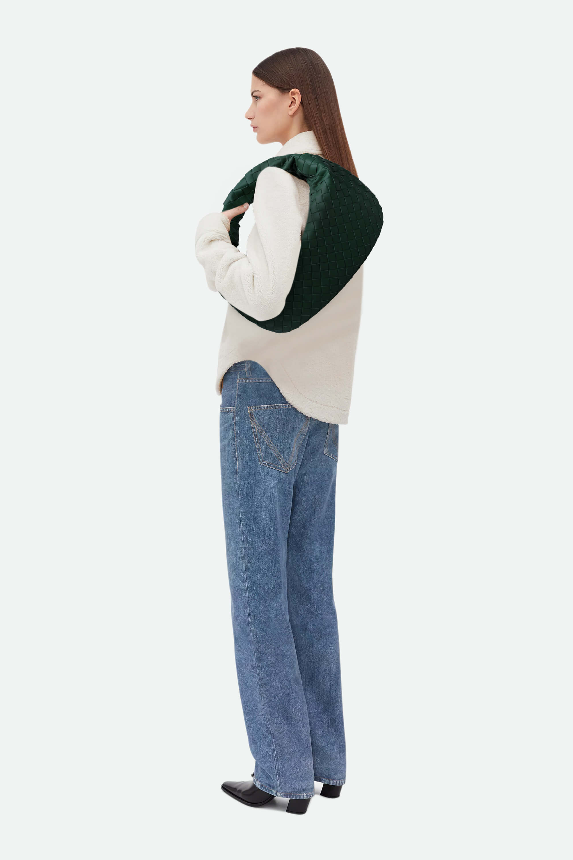 Person wearing a green sweater over a white shirt with blue jeans on a white background