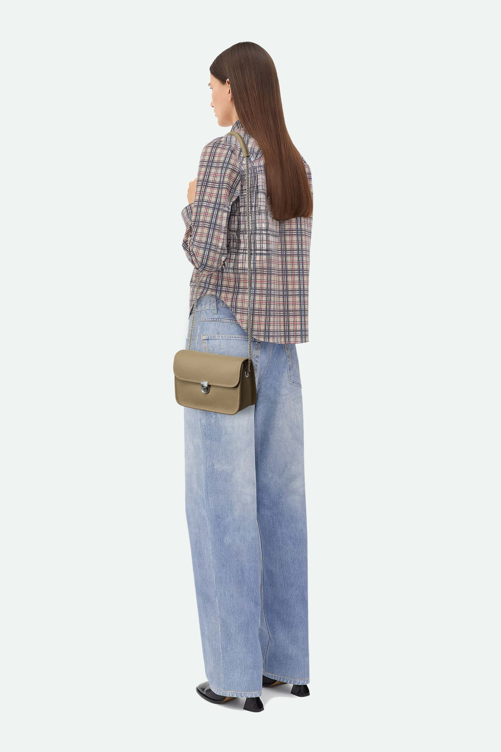 Person wearing a plaid shirt and jeans with a beige handbag on a white background