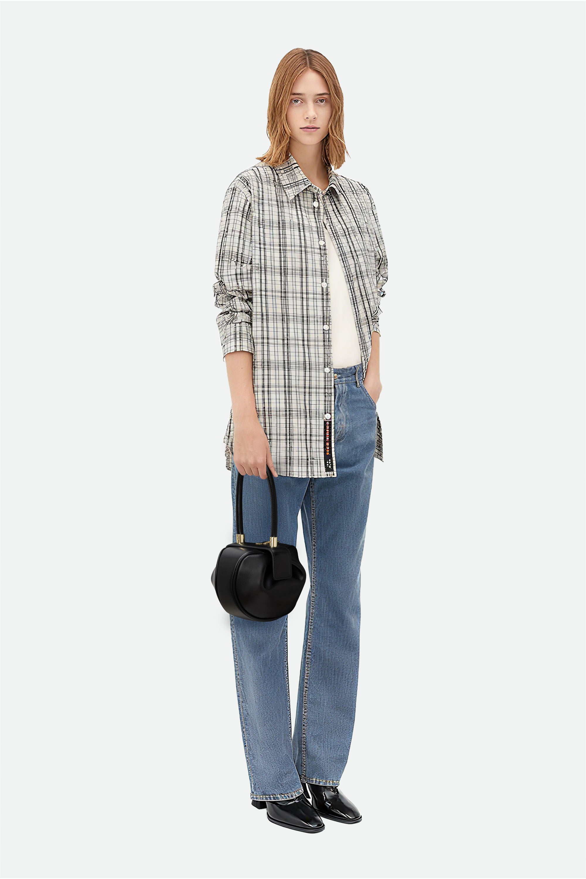 Person wearing a plaid shirt, jeans, and holding a black handbag on a white background