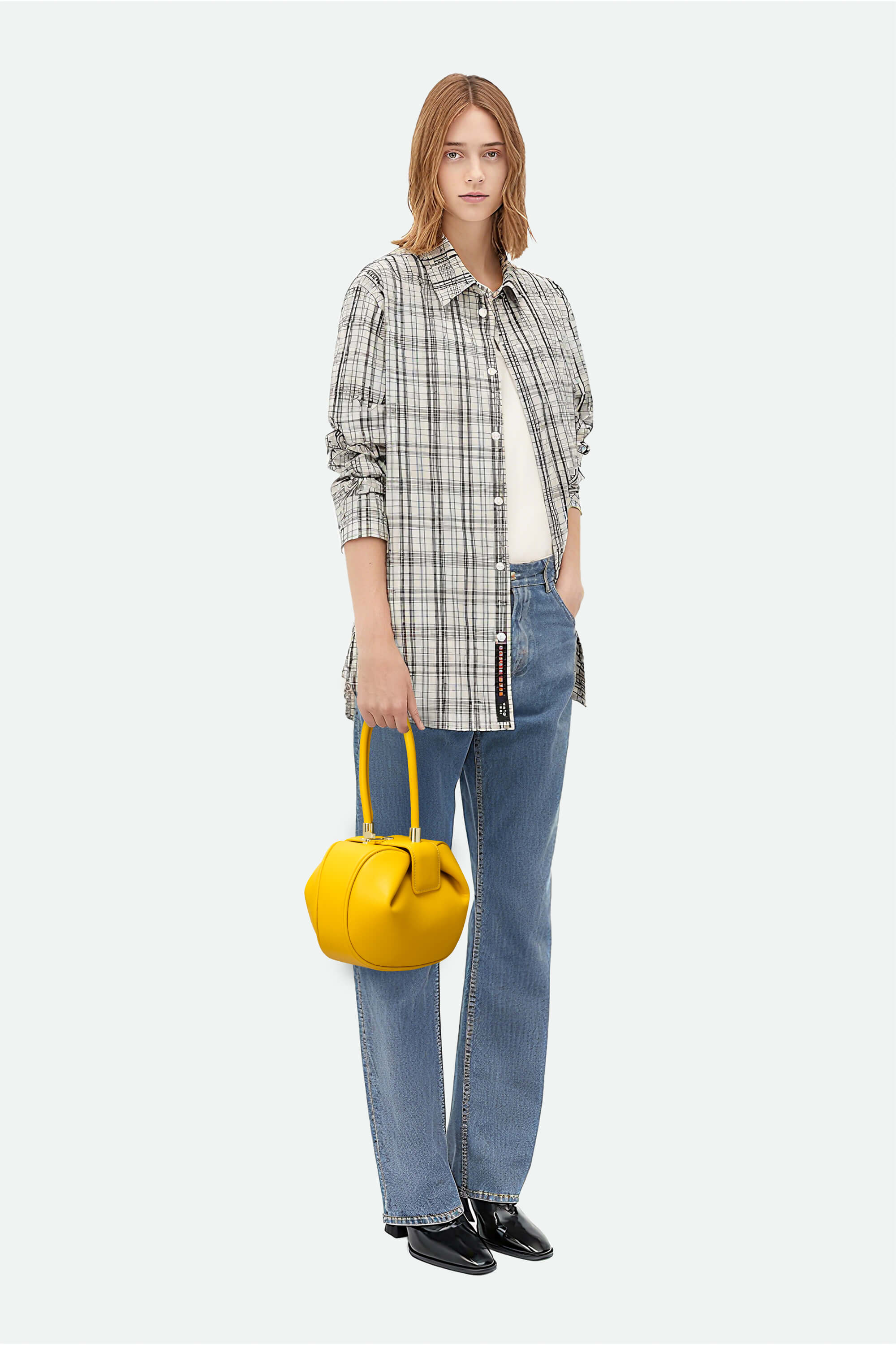 Woman holding a yellow handbag wearing a plaid shirt and jeans on a white background
