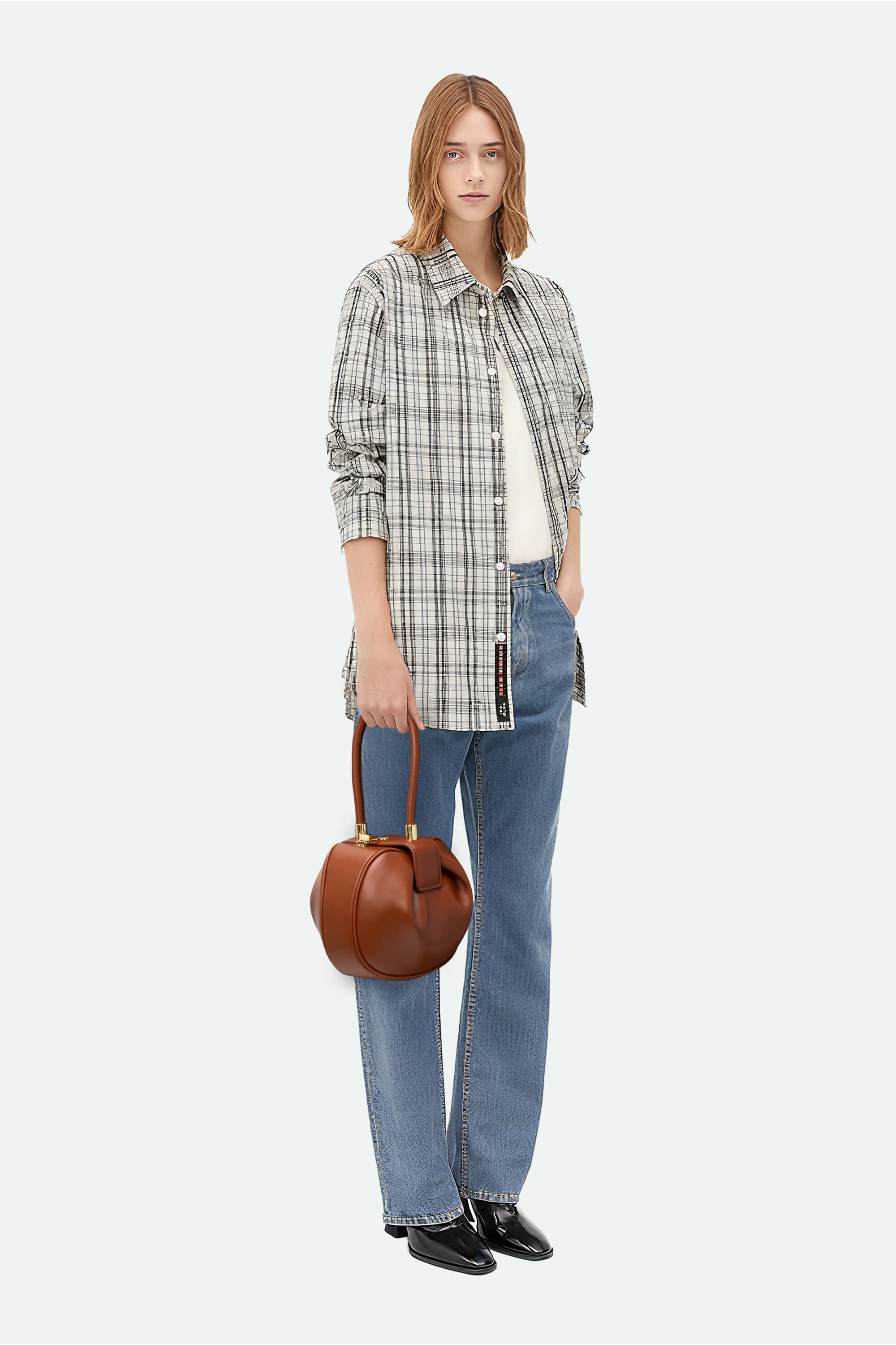 Woman wearing a plaid shirt, jeans, and holding a brown handbag on a white background