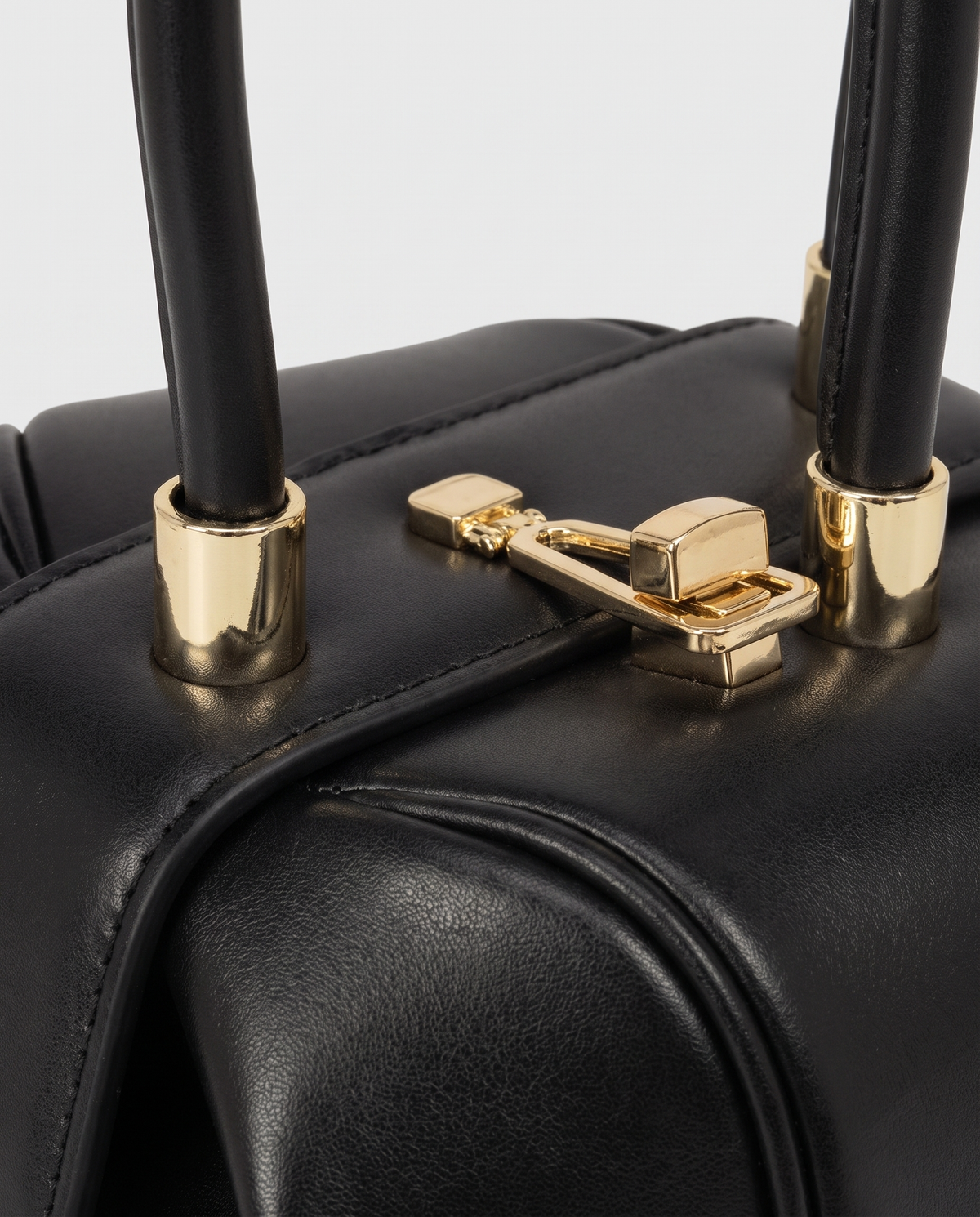 Dumpling Mini leather top-handle bag in Black – close-up of the gold twist-lock and handle fittings