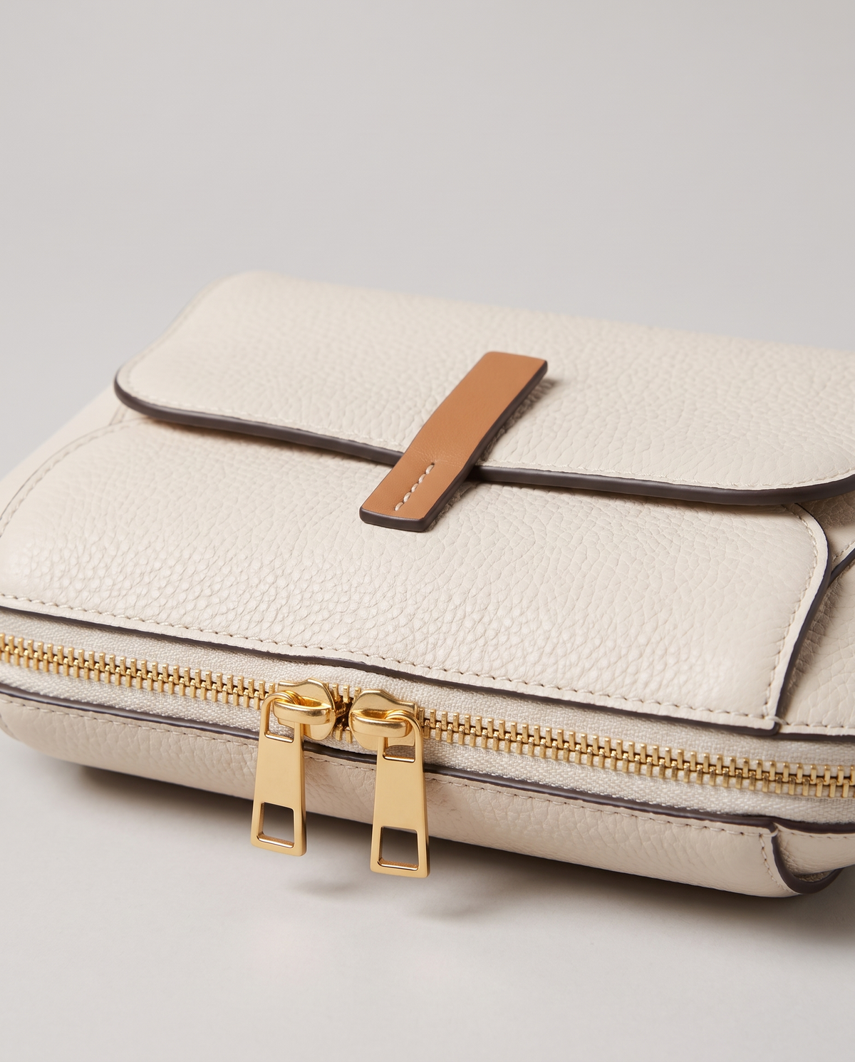 Elara mini leather crossbody in White – close-up of the tan tab, zips and pebbled leather