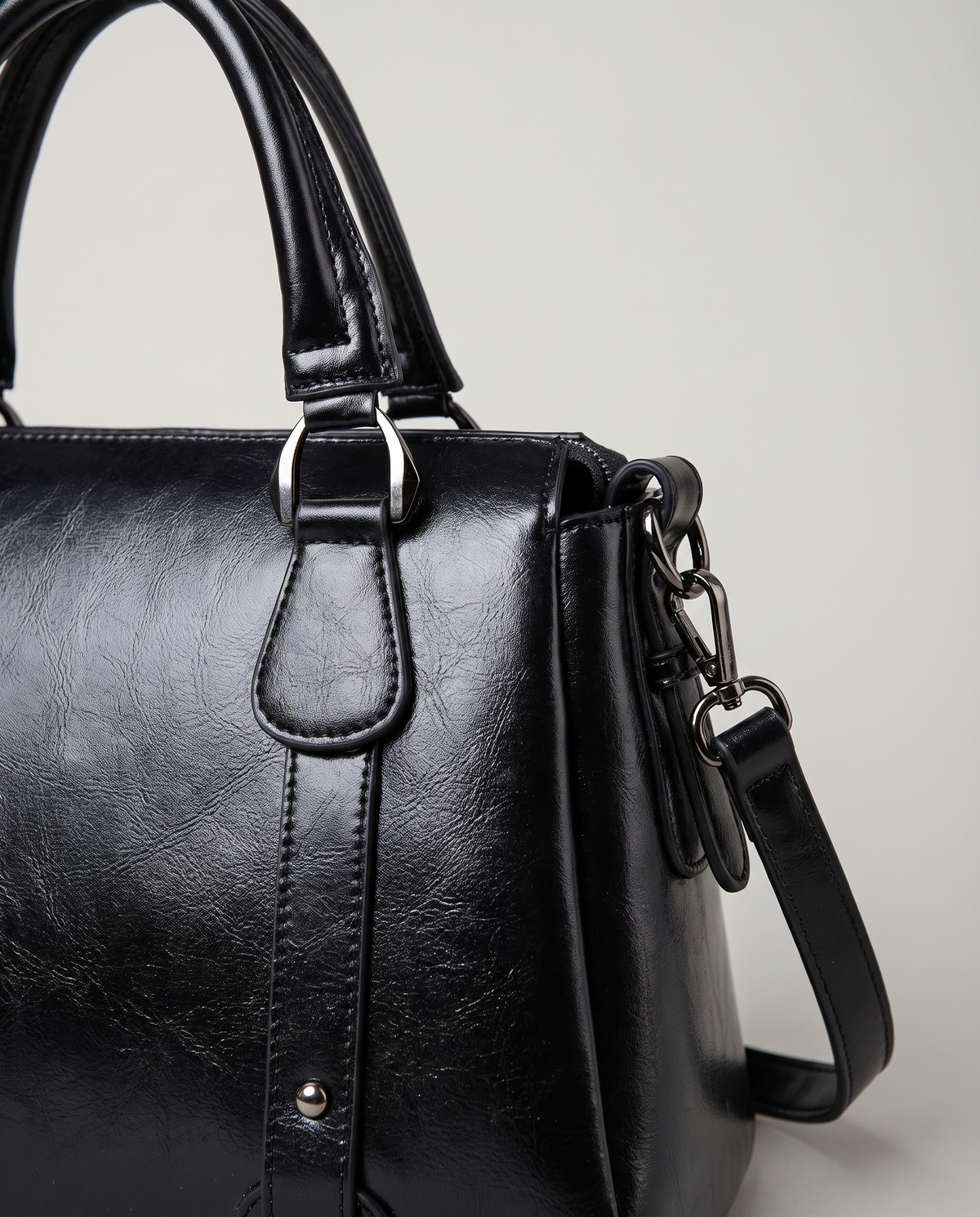 Harlow leather handbag in Black – close-up of the top handle, front strap rivets and side ring