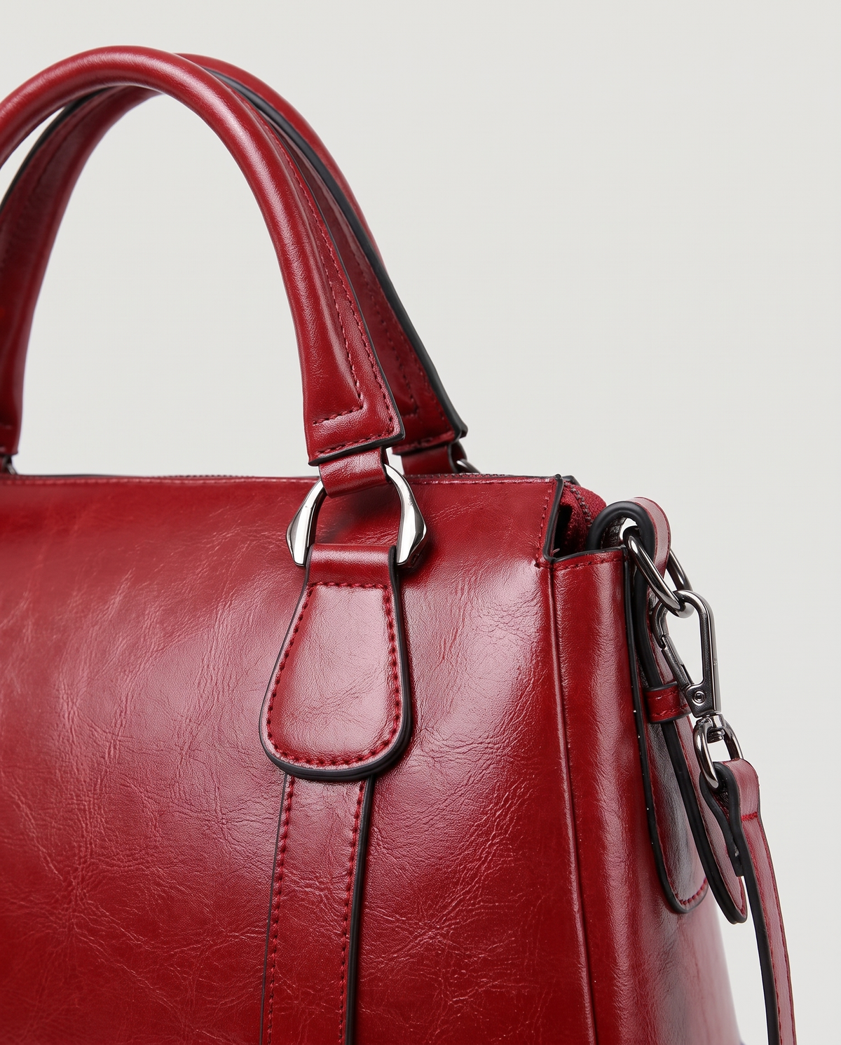 Harlow leather handbag in Red – close-up of the top handle, front strap rivets and side ring