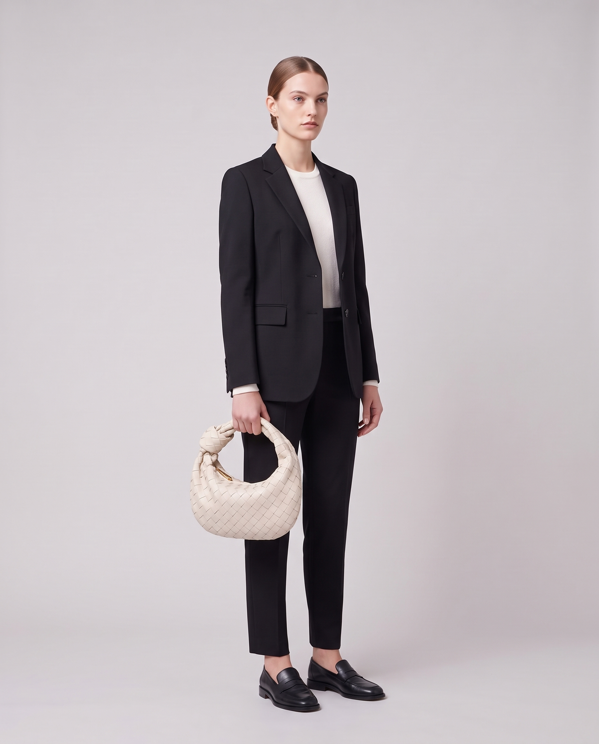 Model carrying the Knot Small woven leather bag in Chalk by its knotted handle