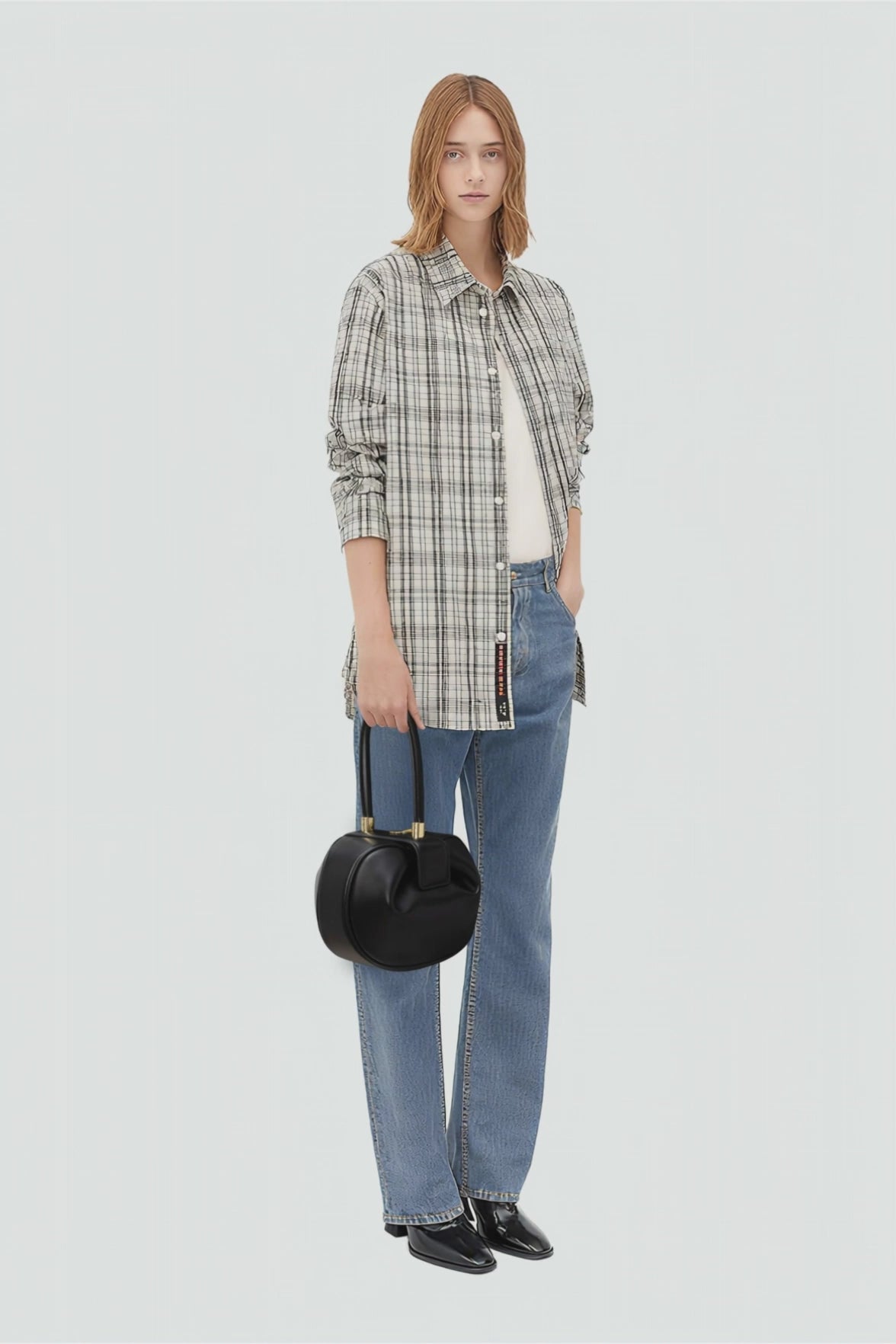 Woman wearing a plaid shirt, jeans, and holding a black handbag on a white background