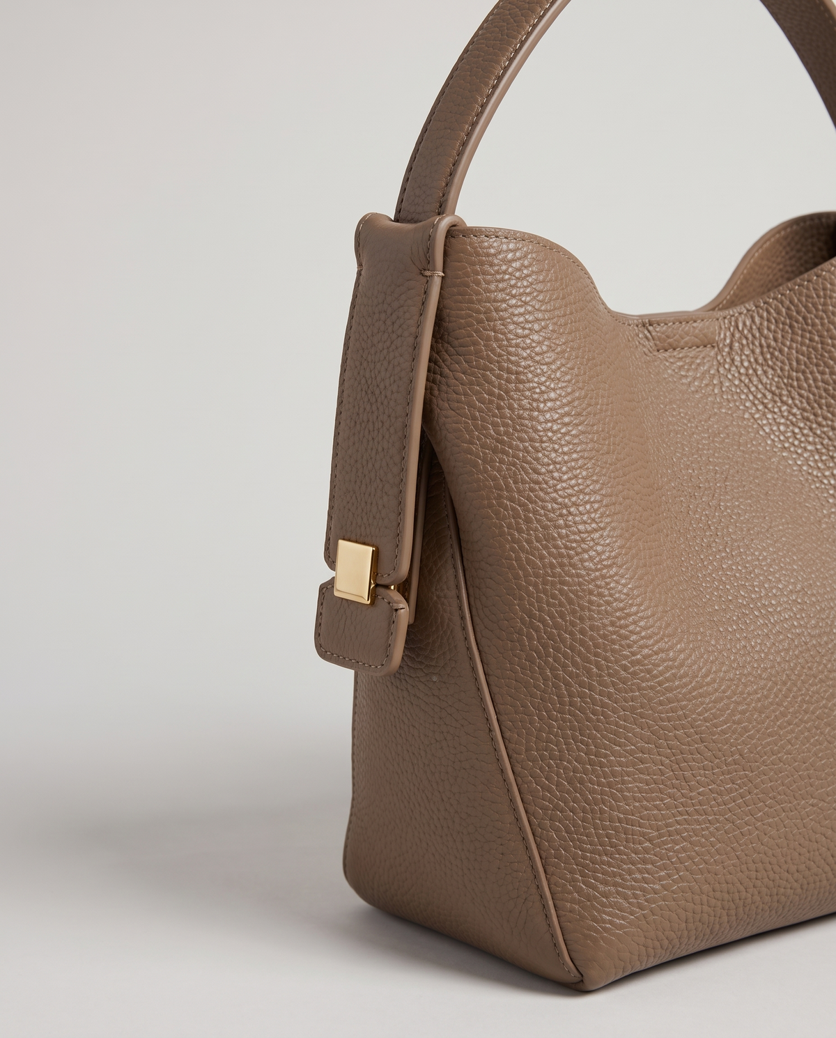 Transit leather bucket bag in Taupe – close-up of the handle tab and gold hardware